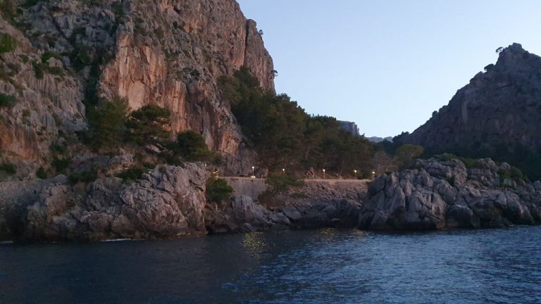 Steile Felsküste mit beleuchteter Uferstraße entlang einer Bucht auf Mallorca in der Abenddämmerung.