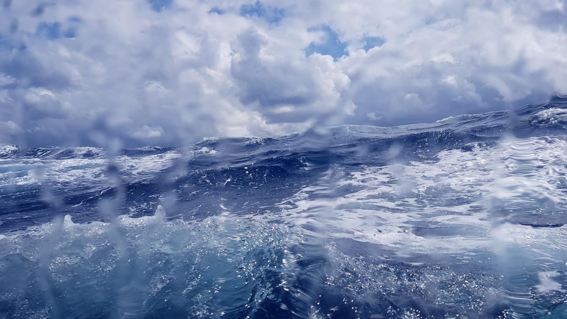 Aufgewühlte Wellen unter dichten Wolken auf offener See, Wassertropfen auf der Kameralinse.