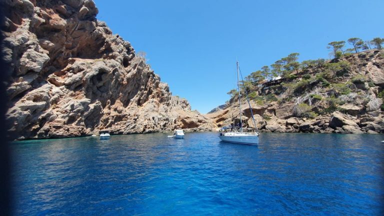 Segelboot ankert in einer schmalen Felsbucht vor Mallorca, umgeben von steilen Klippen mit Pinienbewuchs.