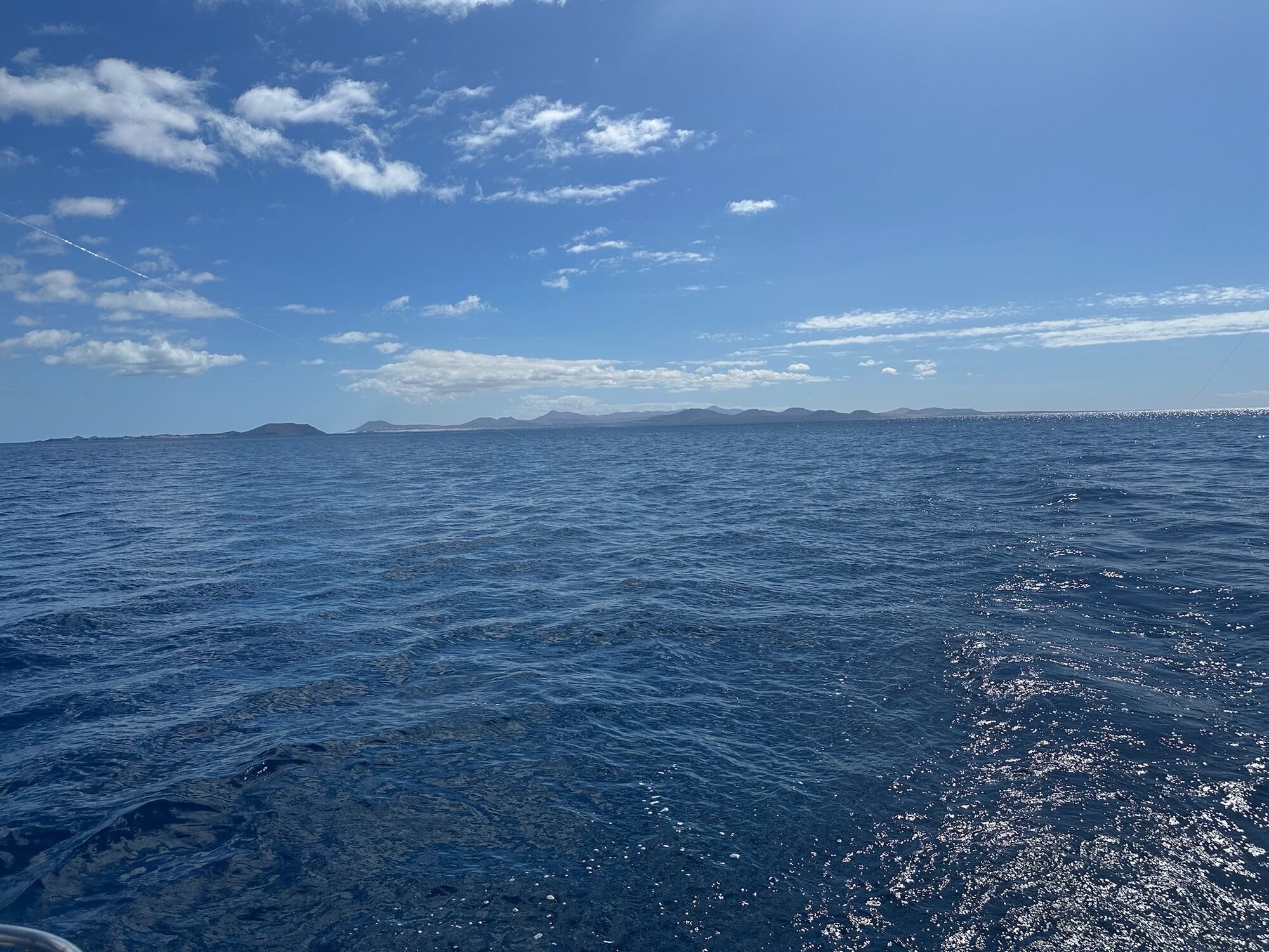 Blick vom Atlantik auf die Vulkanhügel von Lanzarote am Horizont unter blauem Himmel mit Wolken.