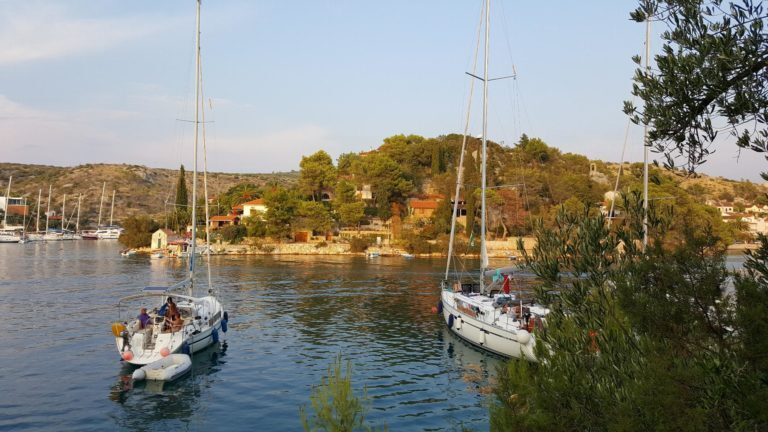 Segelboote ankern in einer Bucht in Dalmatien, Kroatien, umgeben von grünen Hügeln und Steinhäusern.