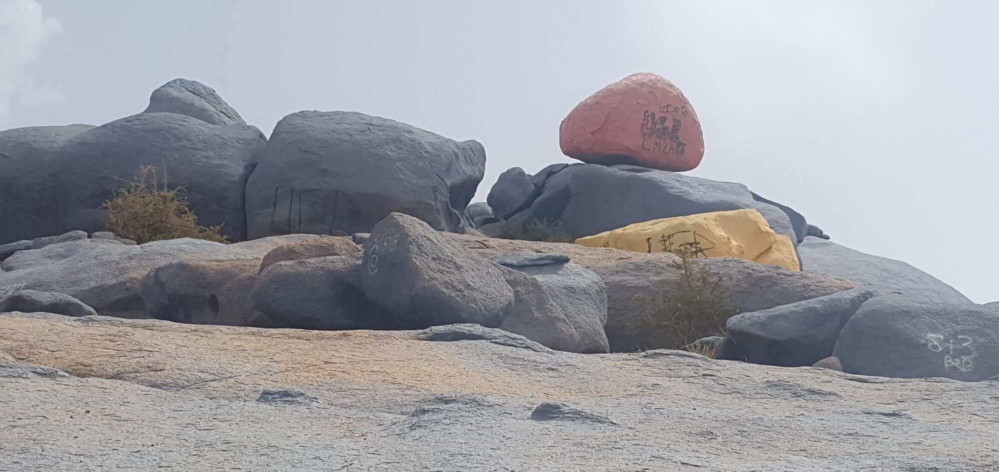 Rosafarbener und gelber Felsbrocken mit Graffiti auf grauen Granitfelsen an der marokkanischen Atlantikküste.