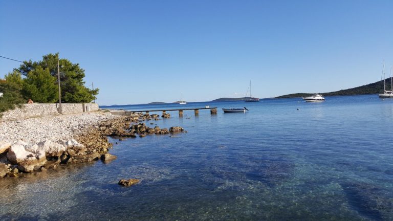 Steinige Bucht mit Steg, Booten und Segelyachten vor den Kornaten in Dalmatien, Kroatien.