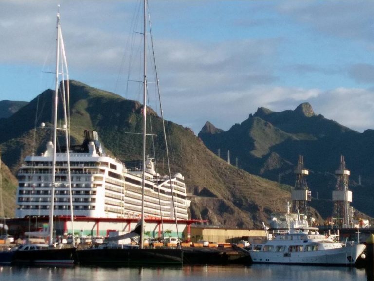 Kreuzfahrtschiff und Segelmasten im Hafen von Teneriffa vor schroffer Bergkulisse.