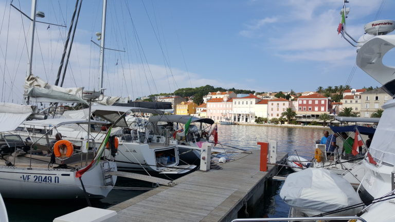 Segelboote liegen im Hafen von Mali Lošinj, im Hintergrund die farbigen Häuser der Uferpromenade.