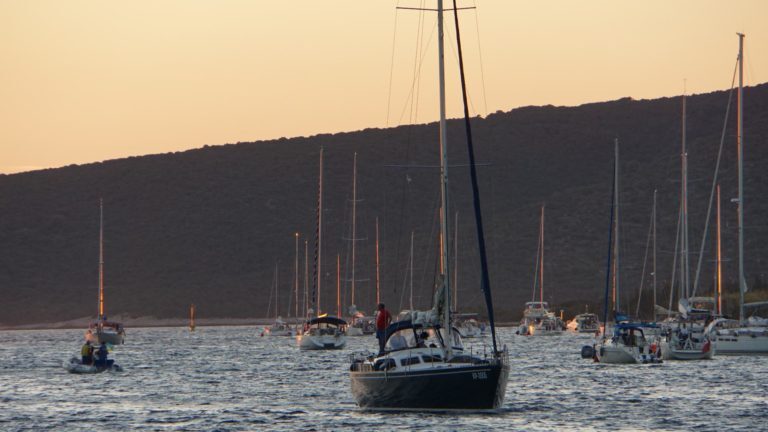Segelboote ankern in einer Bucht vor einer bewaldeten Hügelkette in Kroatien bei Sonnenuntergang.