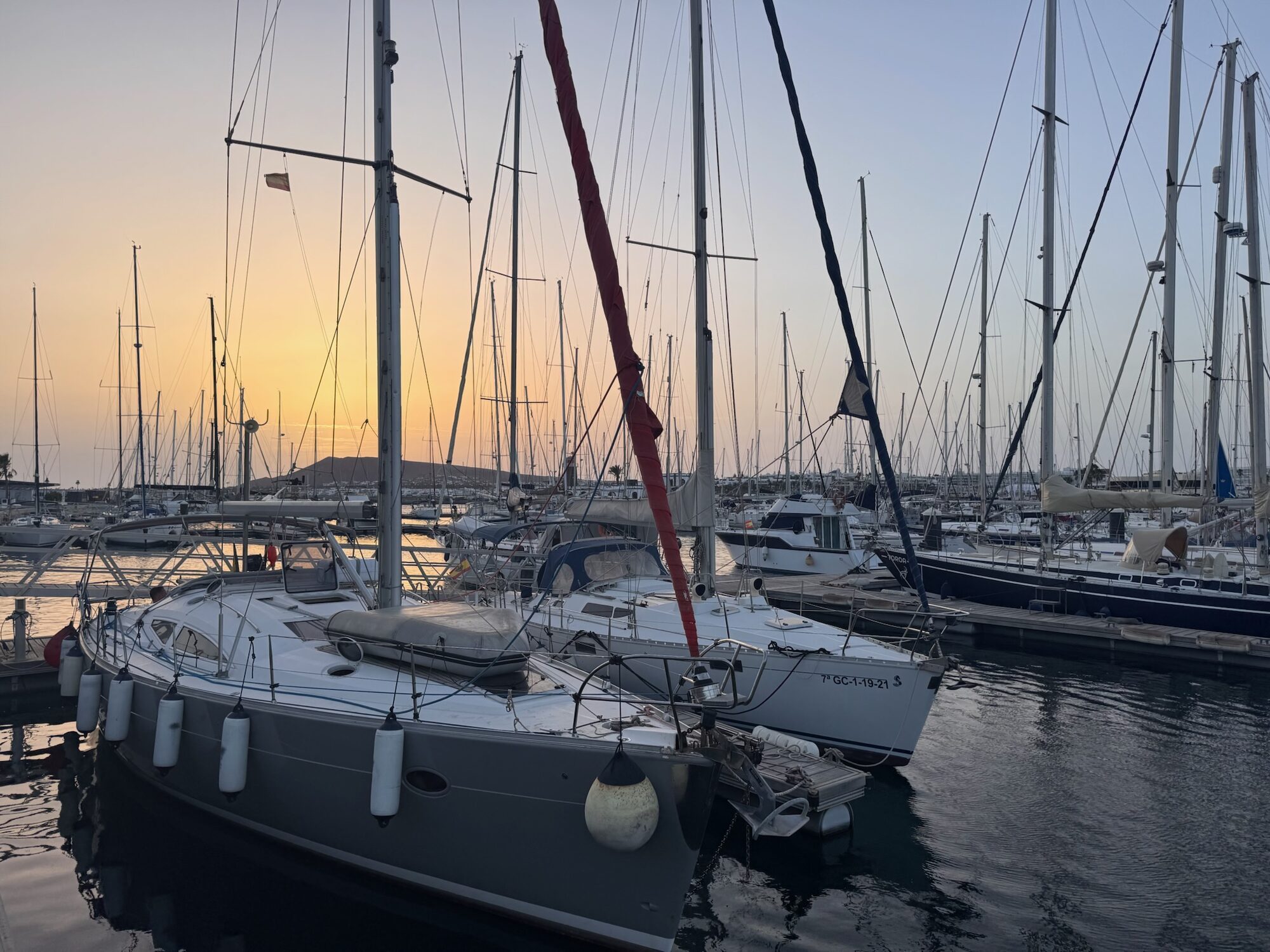 Segelboote liegen bei Sonnenuntergang in der Marina Rubicón auf Lanzarote, im Hintergrund ein Vulkanberg.