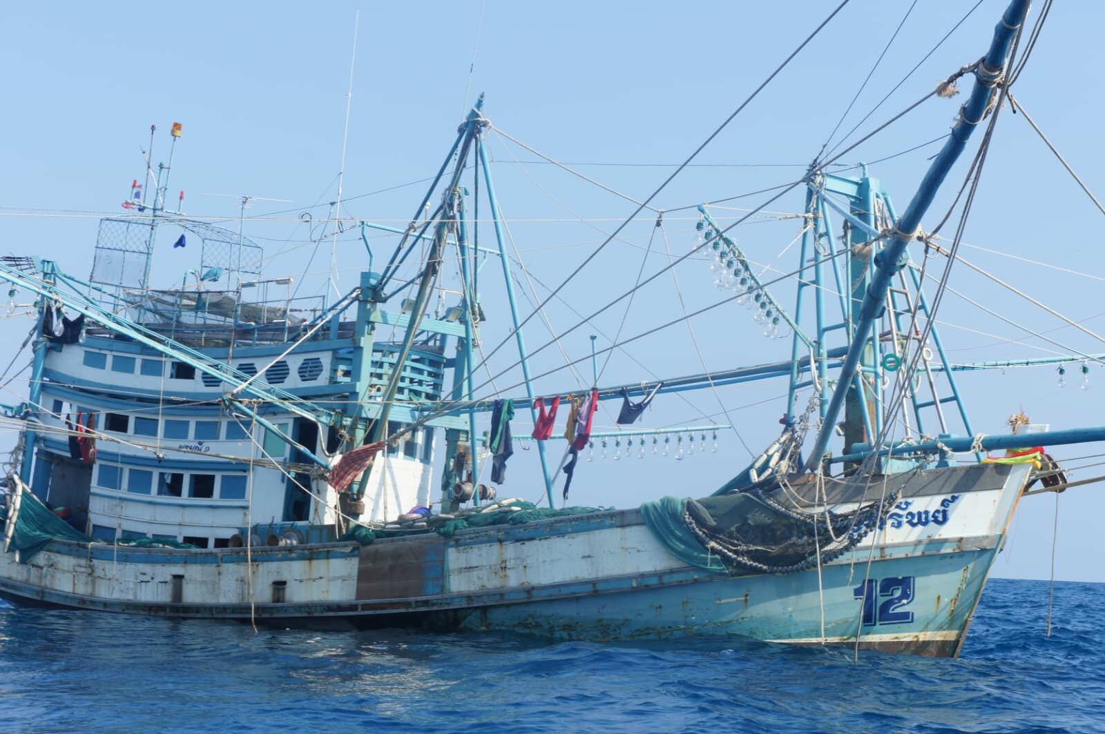 Alter blauer Fischtrawler mit Ausleger-Masten und trocknender Wäsche ankert vor Phuket, Thailand.