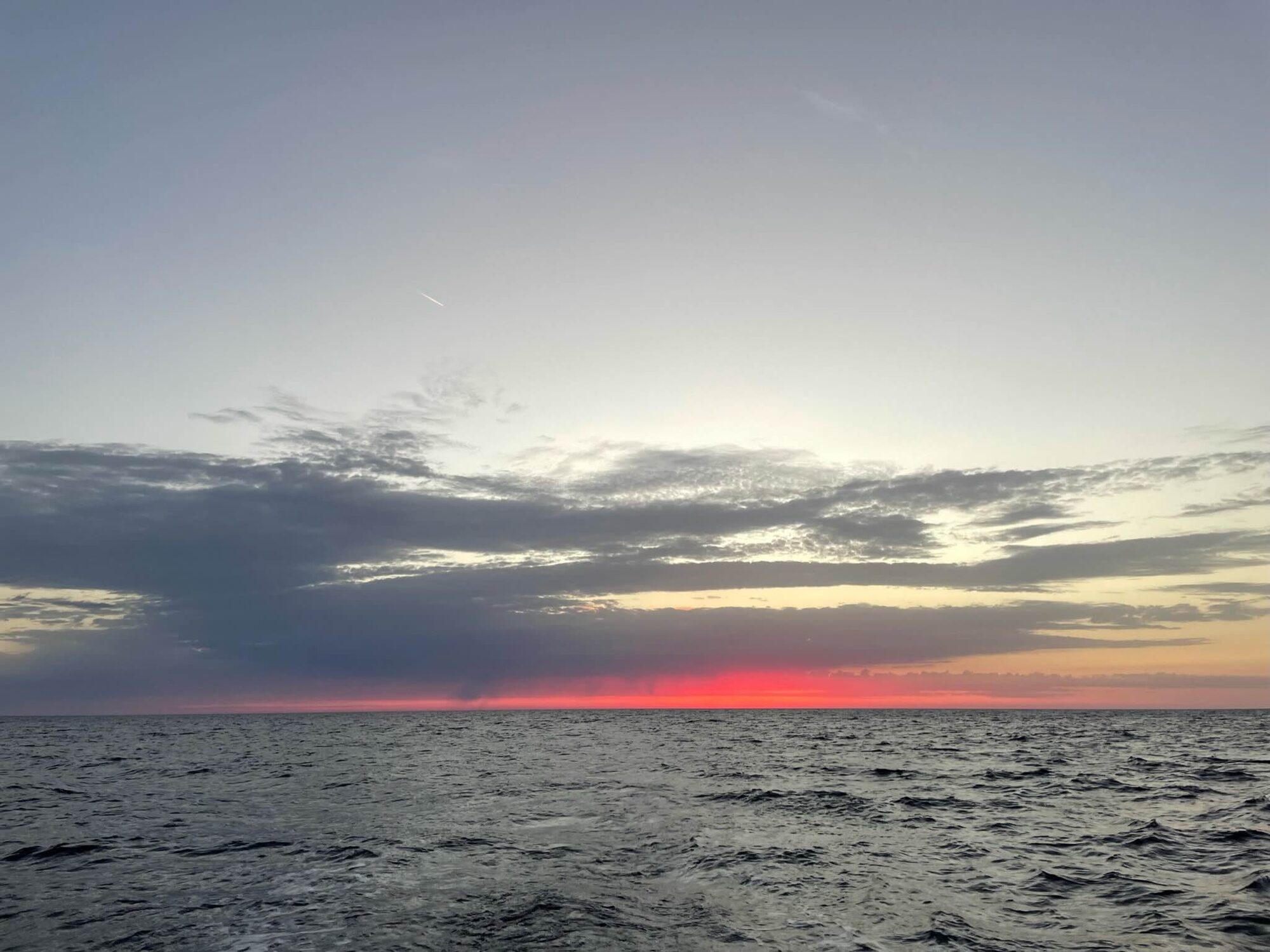Roter Streifen am Horizont über dem offenen Mittelmeer zwischen Mallorca und Sardinien, Wolkenbänder am Himmel.