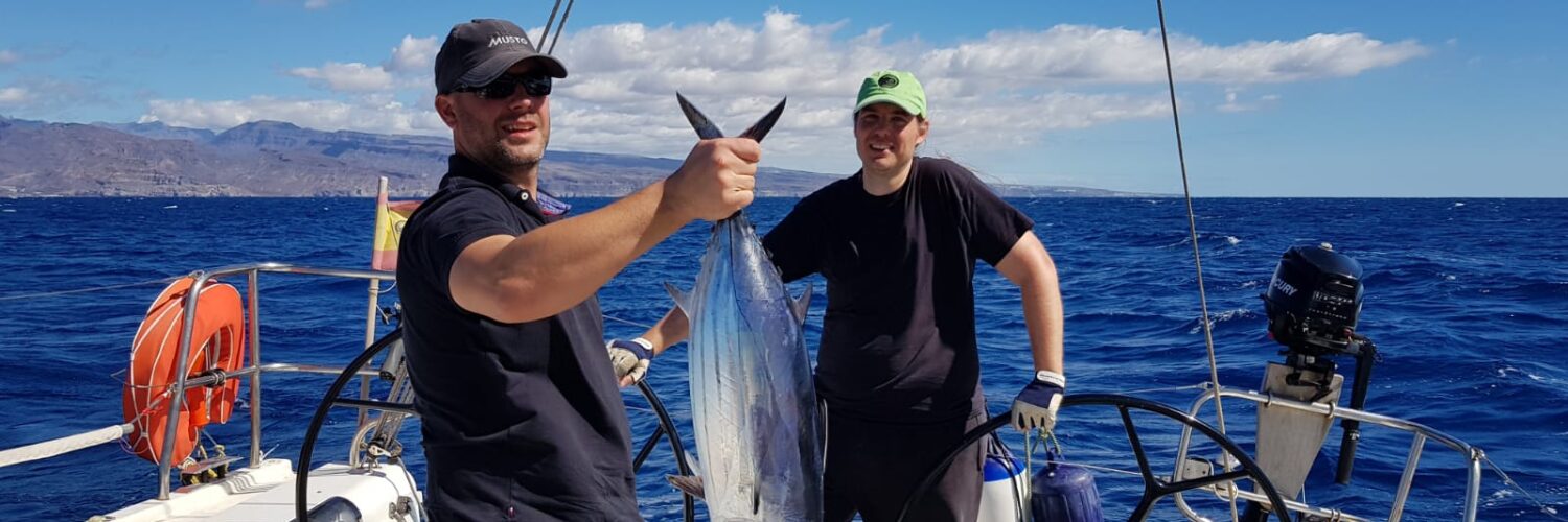 Zwei Männer präsentieren einen frisch gefangenen Thunfisch am Heck eines Segelboots vor der Küste Gran Canarias.