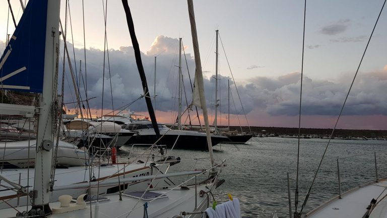 Segelboote liegen dicht an dicht in einem Hafen in Sardinien, während sich Wolken über dem Abendhimmel auftürmen.