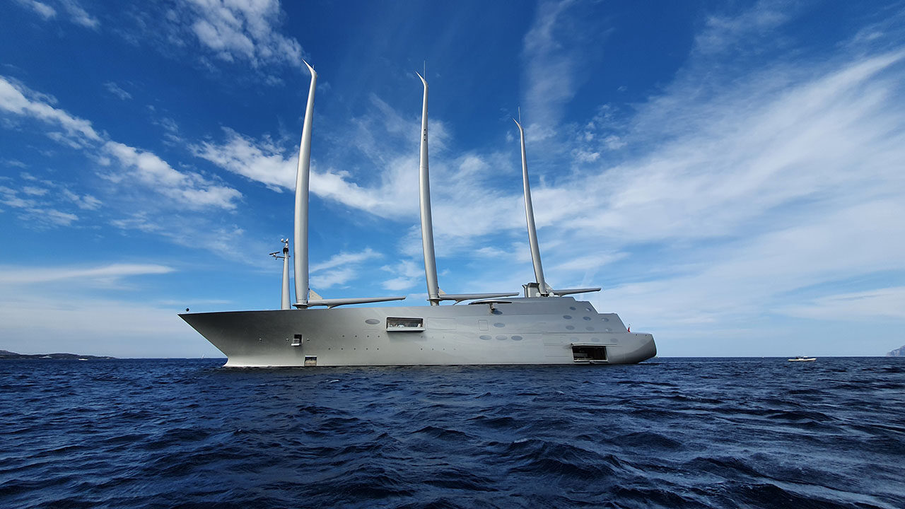 Futuristische Segelyacht mit drei hohen Masten liegt vor Anker im Mittelmeer nahe der Küste.