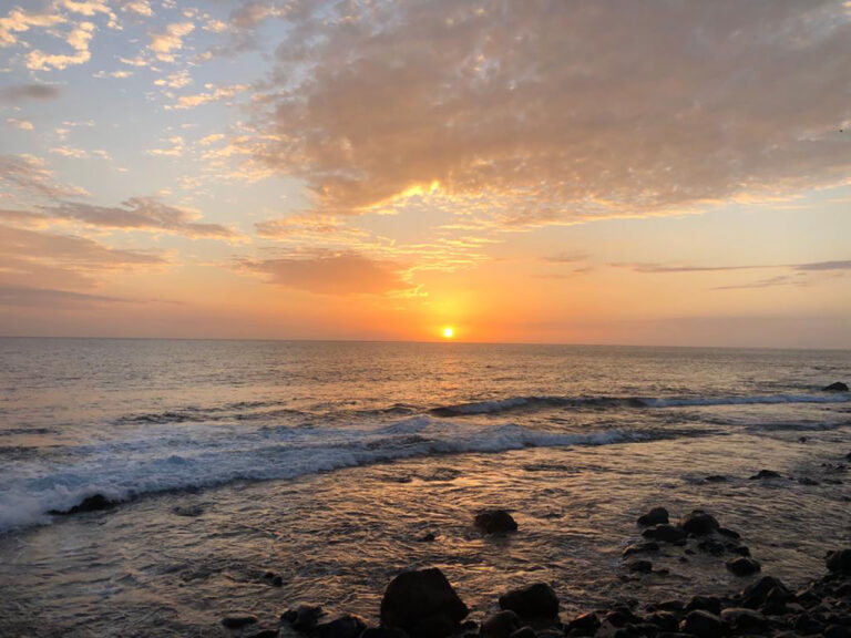 Sonnenuntergang über dem Meer an der felsigen Küste Sardiniens, Wellen brechen sich am Ufer.