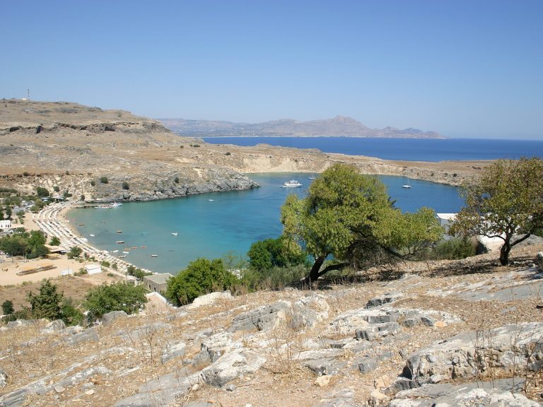Bucht mit türkisfarbenem Wasser und Sandstrand bei Lindos auf Rhodos, umgeben von kargen Hügeln.