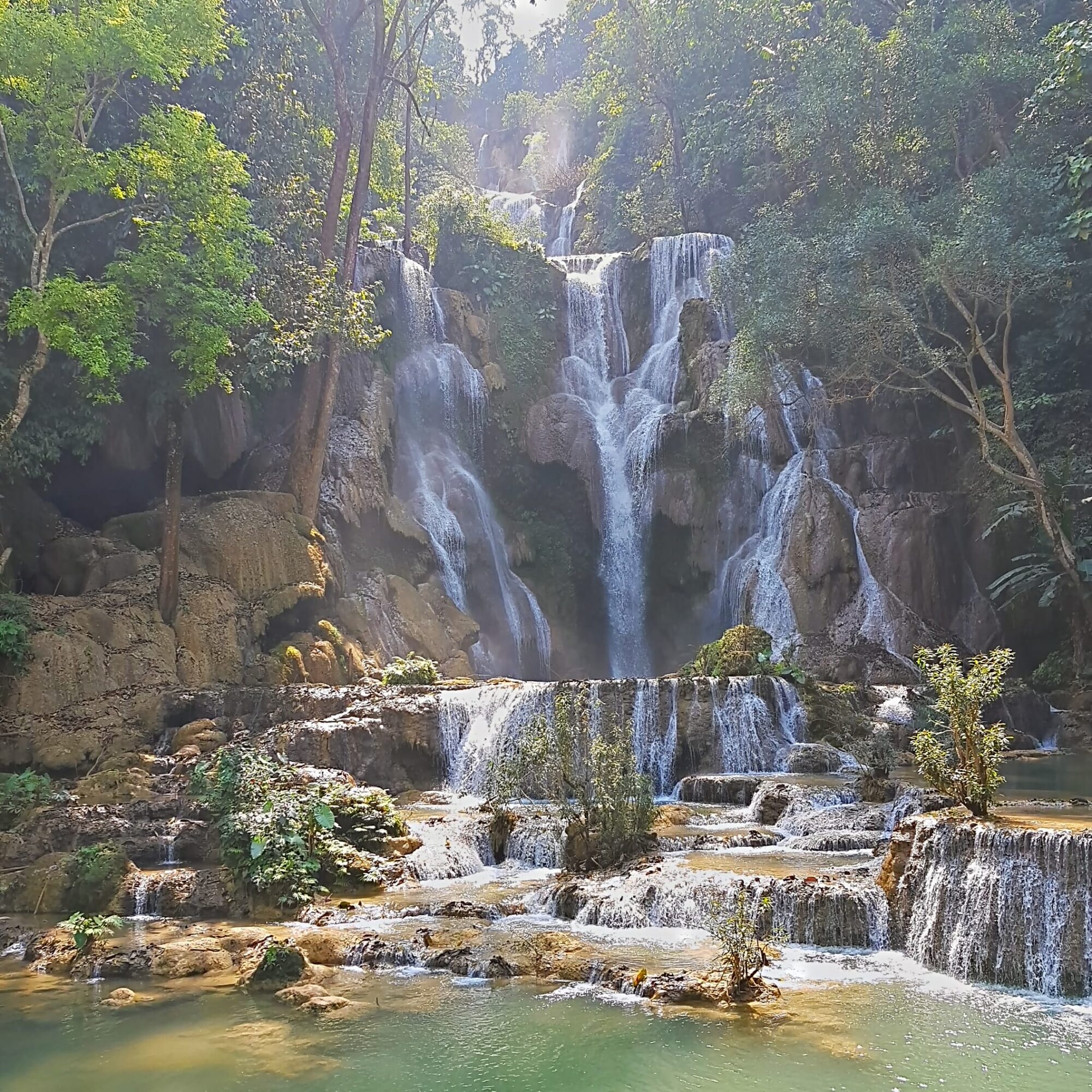 Mehrstufiger Wasserfall stürzt über Kalksteinterrassen in türkise Becken, umgeben von dichtem Dschungel.