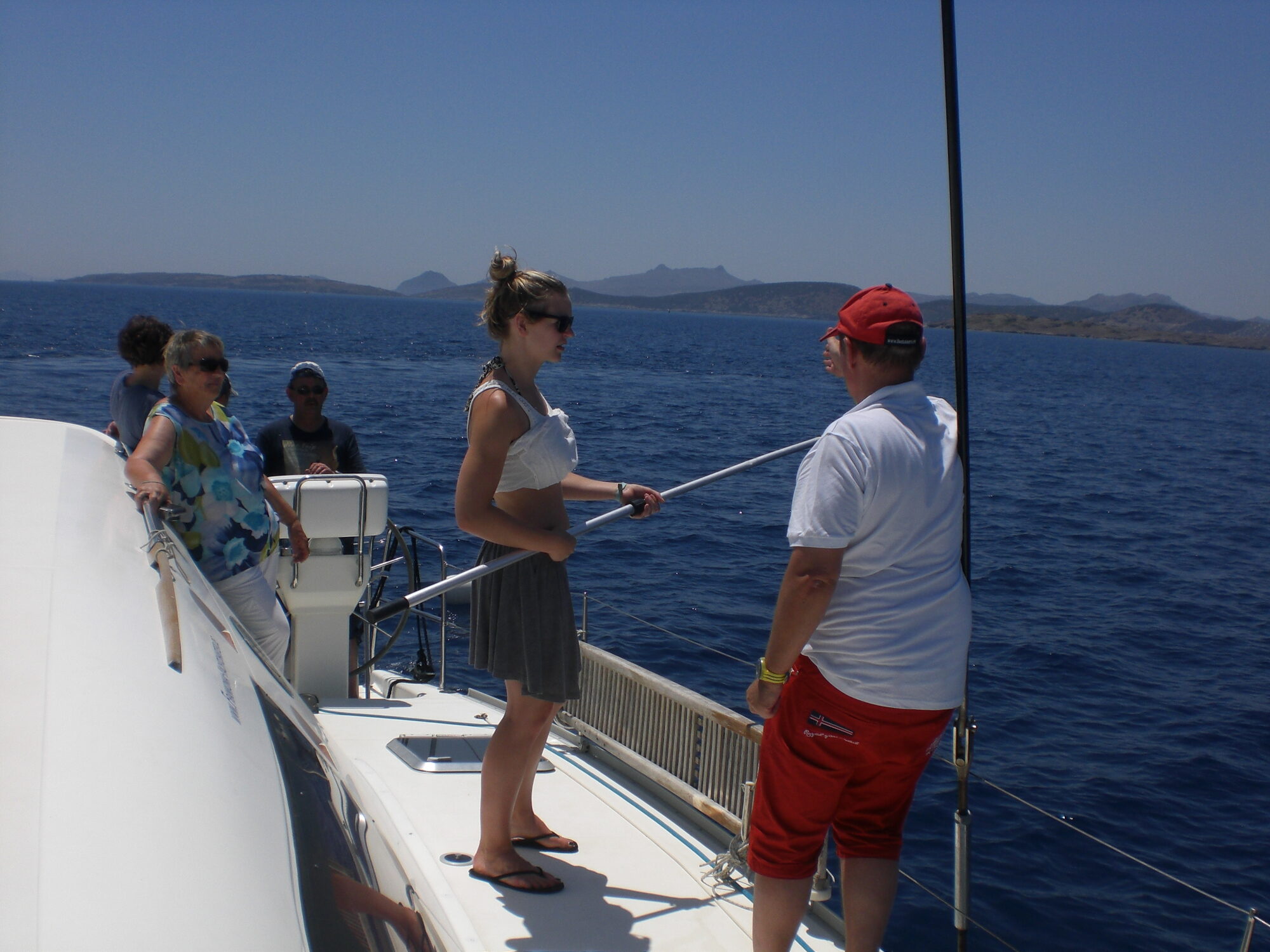 Passagiere stehen an Deck eines Segelboots in der Ägäis vor der türkischen Küste, im Hintergrund Inseln.