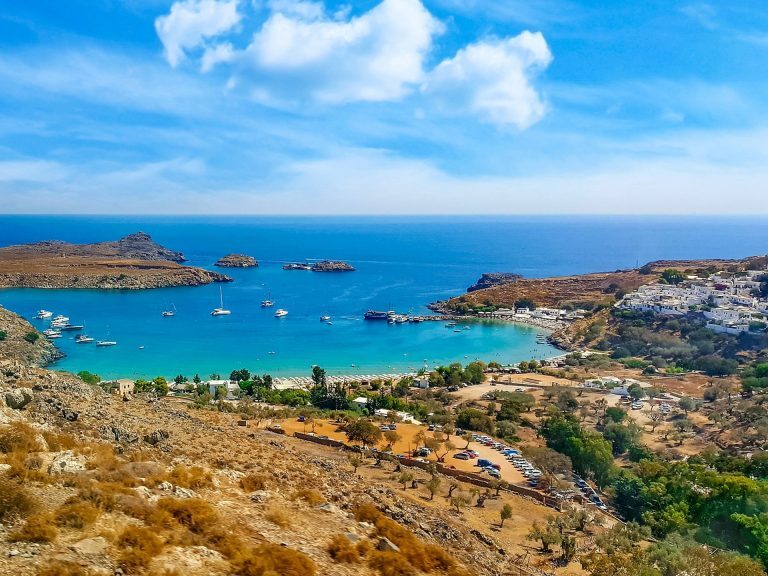 Bucht von Lindos auf Rhodos mit türkisem Wasser, ankernden Segelbooten und weißen Häusern am Ufer.