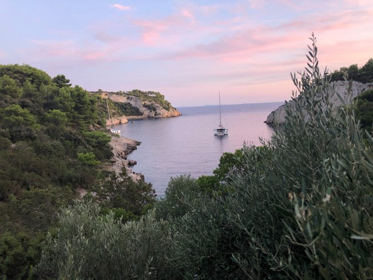 Ein Katamaran ankert in einer felsigen, bewaldeten Bucht an der kroatischen Küste in den Kornaten.