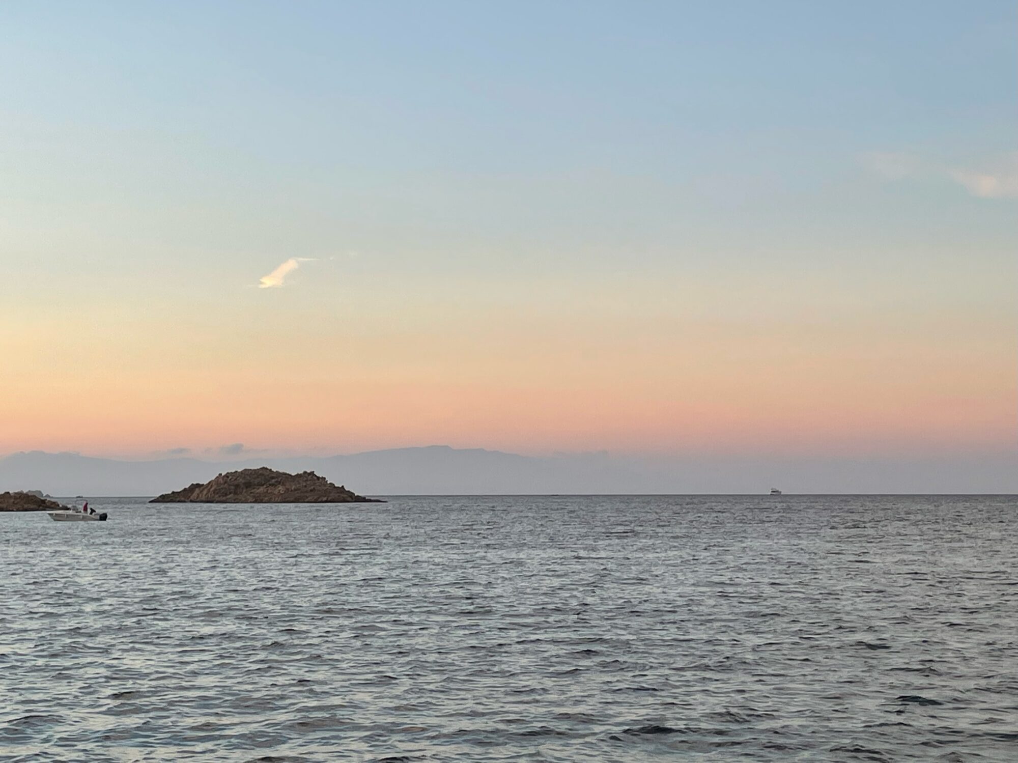 Kleine Felseninsel vor der sardischen Küste im Abendlicht, mit einem Boot und Bergen im Hintergrund.