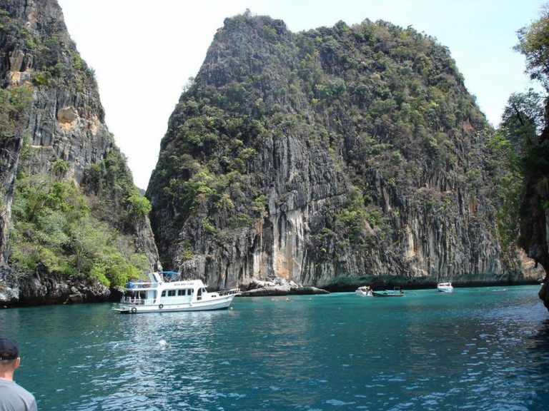 Boote ankern in einer türkisfarbenen Bucht zwischen steilen, bewaldeten Kalksteinfelsen in Krabi.