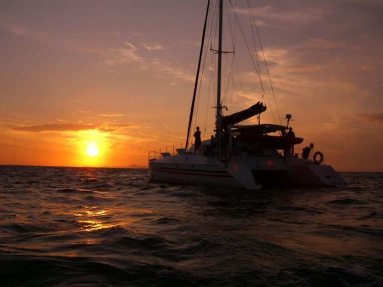 Katamaran mit Personen an Deck bei Sonnenuntergang auf dem Meer vor Phuket.