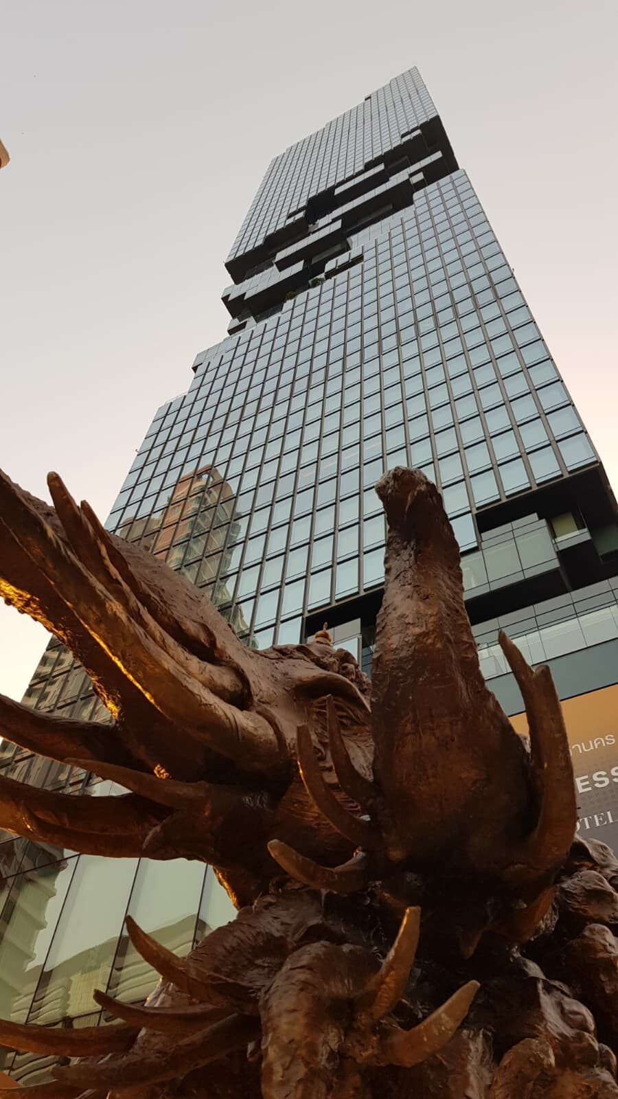 Bronzeskulptur mit klauenartigen Formen vor einem Hochhaus mit ausgeschnittenem Muster in der Fassade, Bangkok.