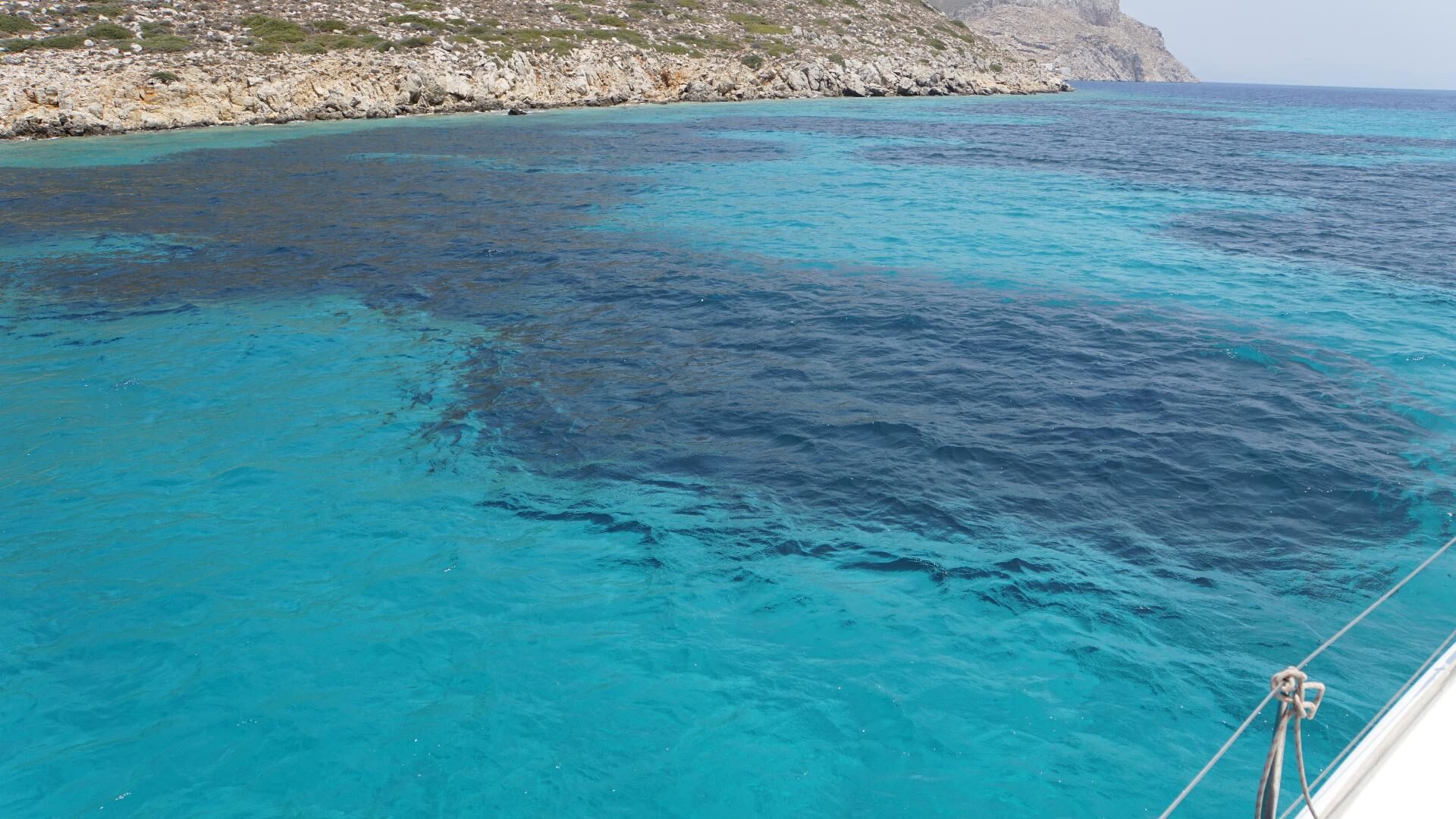 Türkisfarbenes Wasser vor felsiger Küste Mallorcas, im Vordergrund Bug und Tau eines Segelboots.