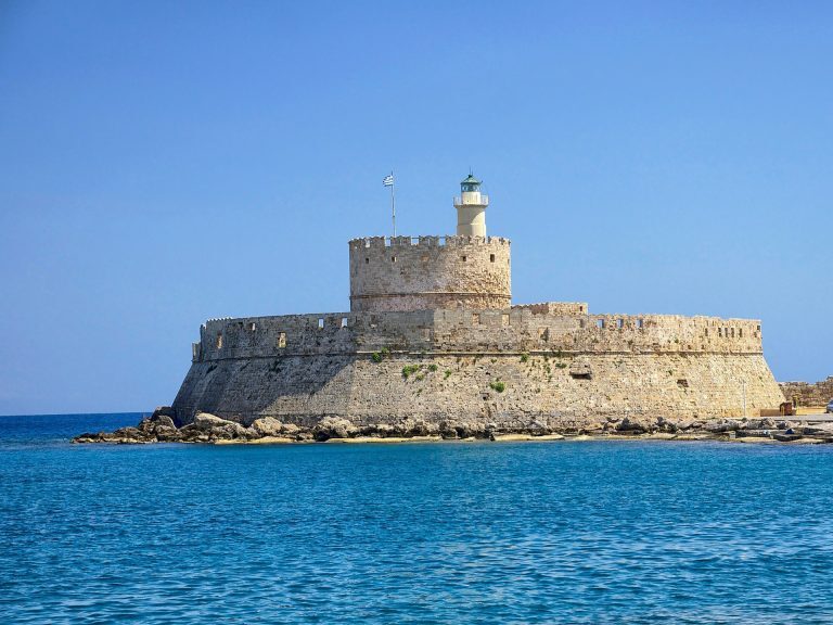 Die Festung mit Leuchtturm von Agios Nikolaos ragt am Hafeneingang von Rhodos aus dem türkisblauen Meer.