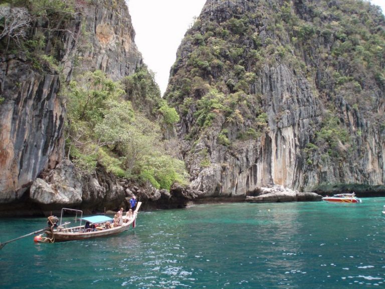 Longtail-Boote vor schroffen Kalksteinfelsen in der türkisfarbenen Bucht bei Phuket, Thailand.
