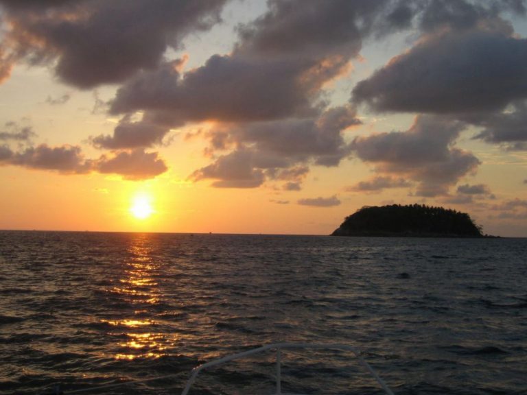 Sonnenuntergang über der Andamanensee vor Phuket, mit einer bewaldeten Insel am Horizont.