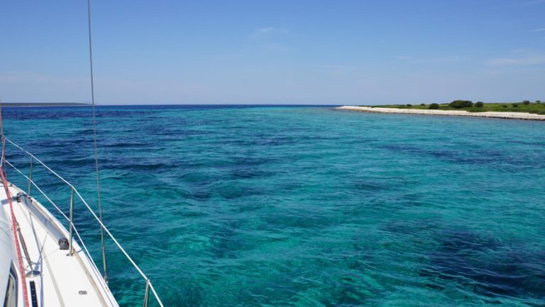 Segelboot fährt durch türkisfarbenes Wasser vor einer flachen Insel in den Kornaten, Kroatien.