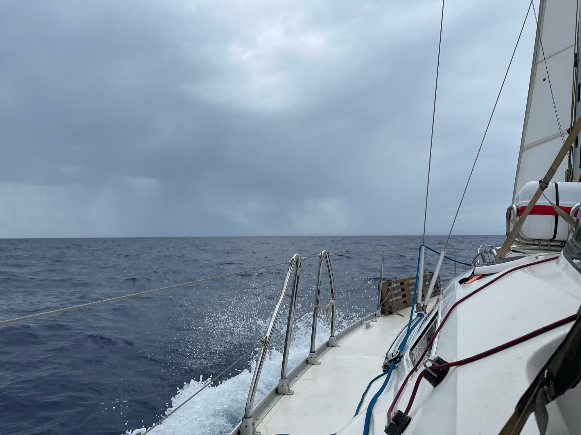 Segelboot durchquert bei bewölktem Himmel den Atlantik, Bug schneidet durch Wellen mit aufspritzender Gischt.