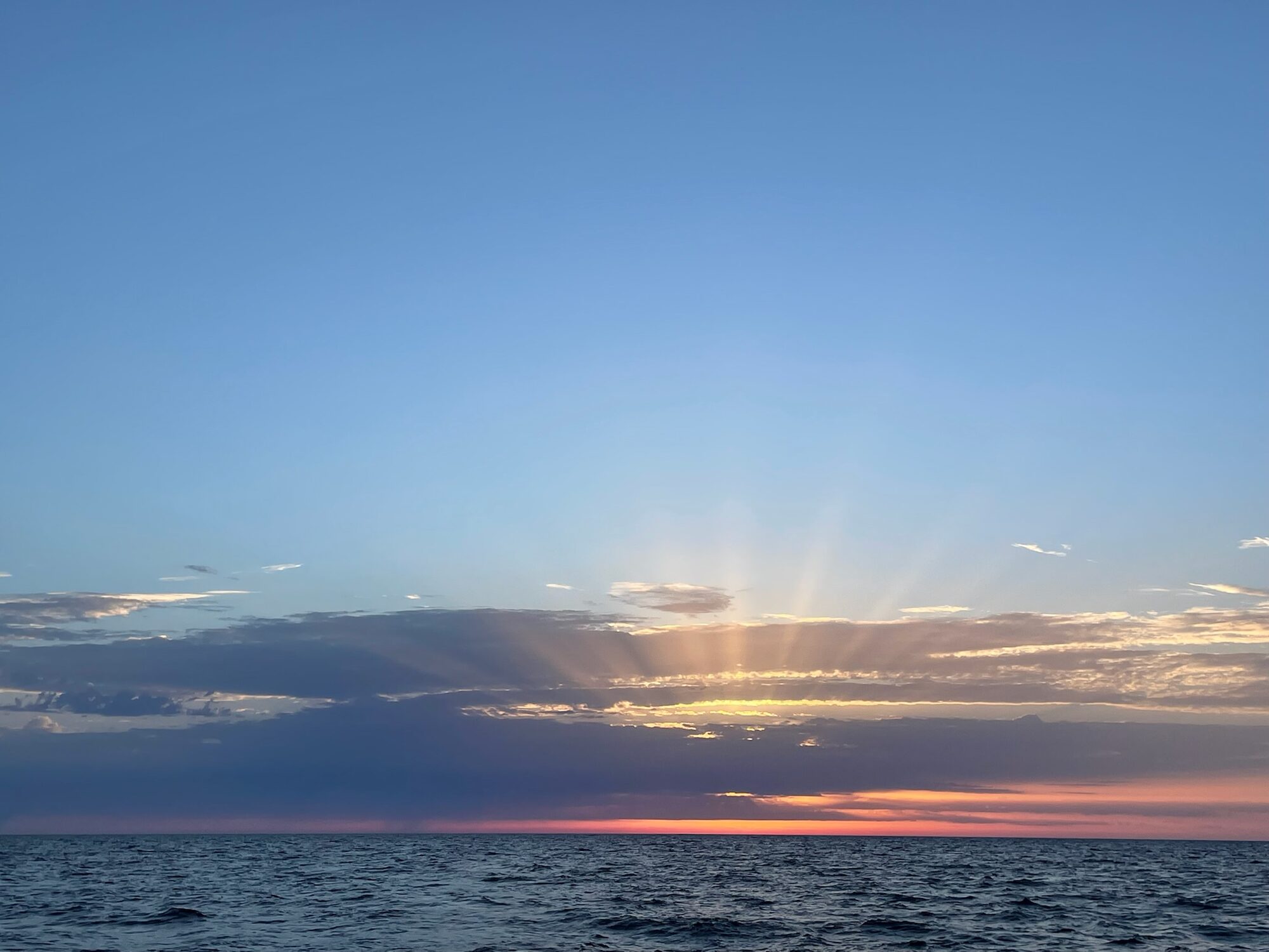 Sonnenuntergang mit Strahlenkranz hinter Wolkenbändern über dem Atlantik, gesehen von Bord während des Törns.