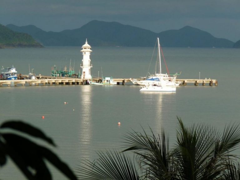 Segelboot liegt an einem Pier mit Leuchtturm vor bewaldeten Inseln in der Phang-Nga-Bucht bei Krabi.
