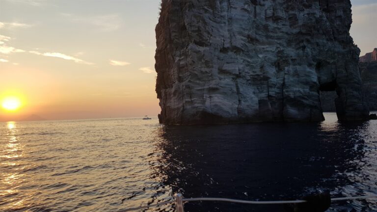 Ein steiler Felsen ragt aus dem Meer der Liparischen Inseln, während die Sonne am Horizont untergeht.