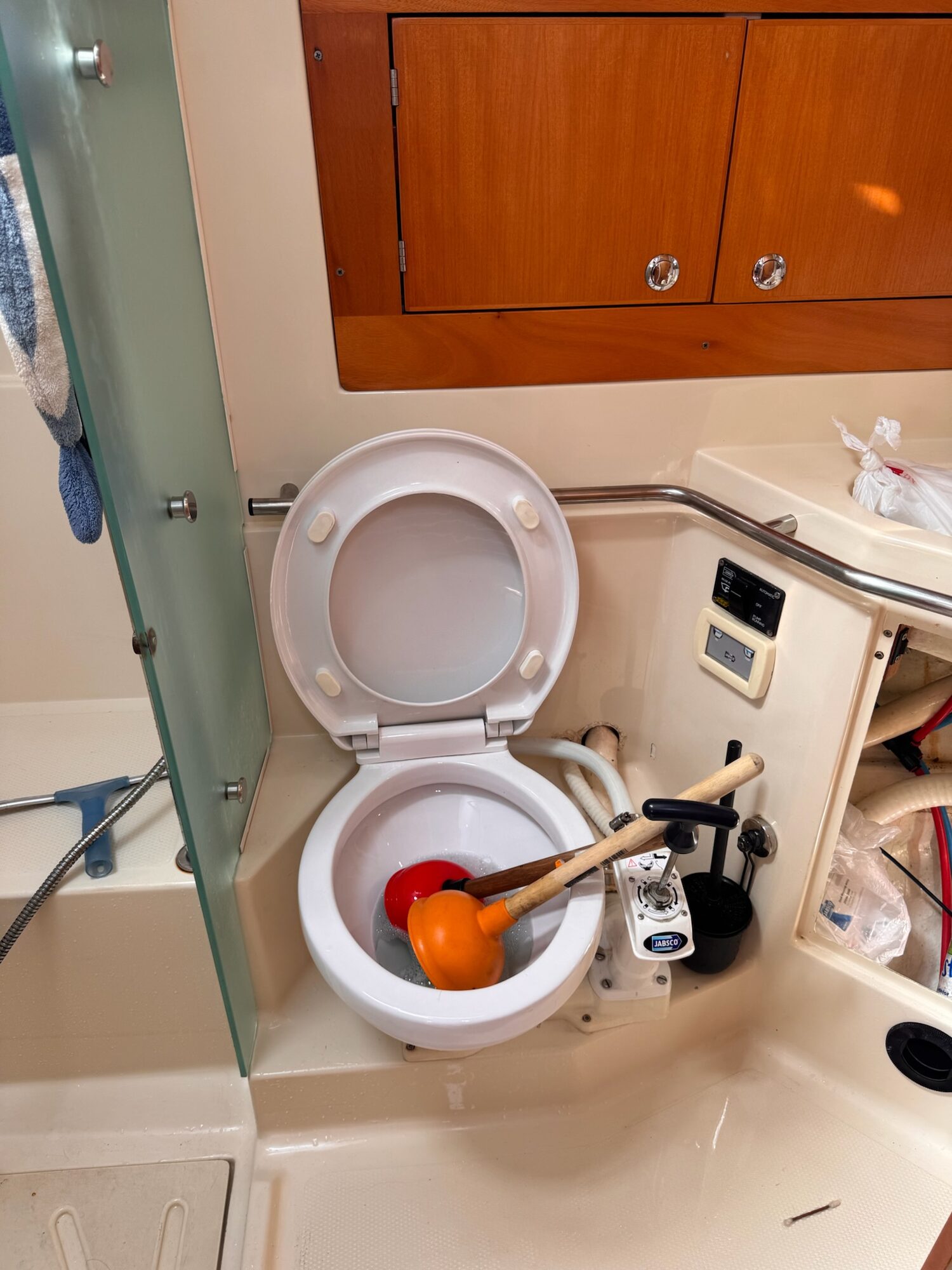 Bordtoilette in einem Bootsbad mit Jabsco-Handpumpe, daneben stecken zwei Saugglocken in der Schüssel.
