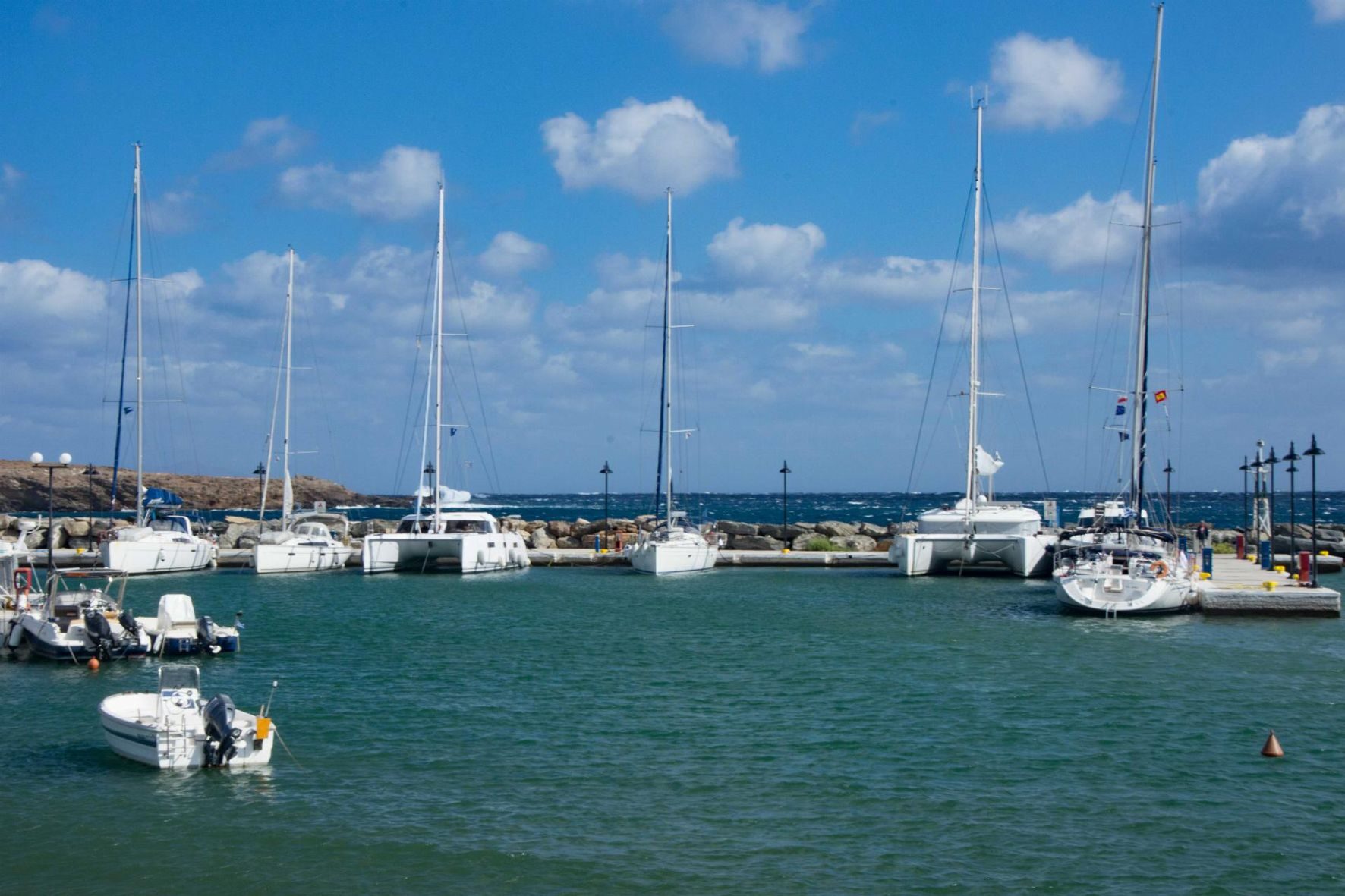 Segelboote und Motorboote liegen an Stegen im Hafen vor türkisem Wasser unter blauem Himmel.