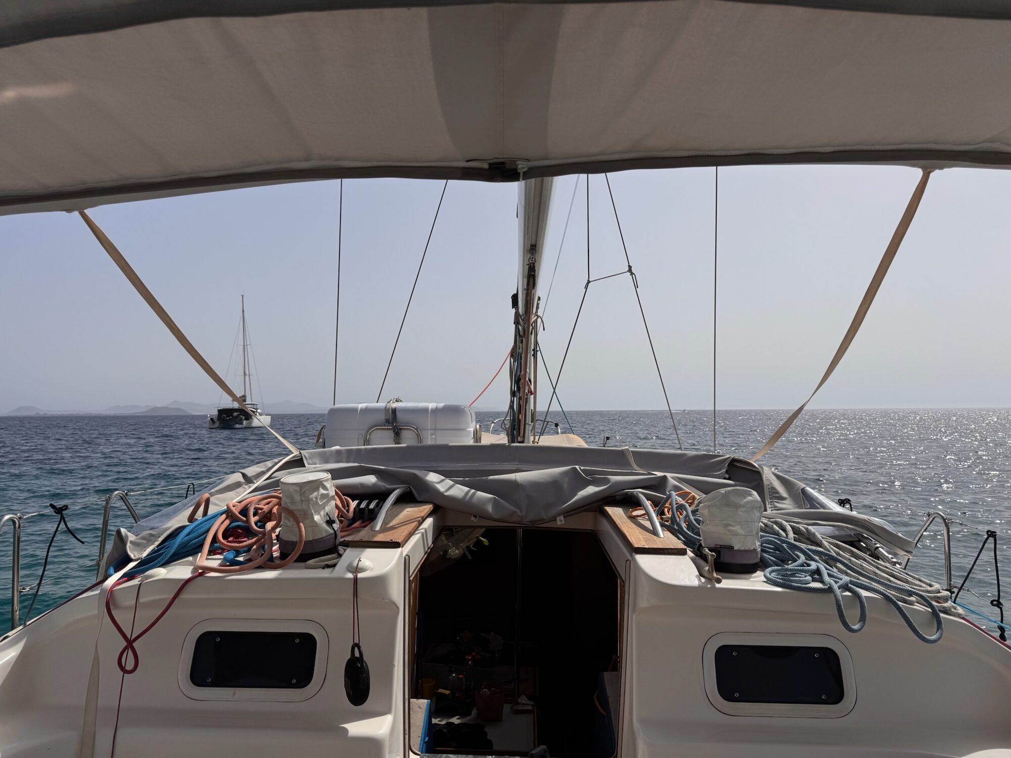 Blick vom Cockpit einer Segelyacht über den Bug auf den Atlantik vor den Kanarischen Inseln, mit einem Katamaran am Horizont.