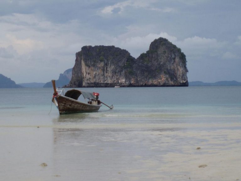 Ein Longtail-Boot liegt vor einem zerklüfteten Kalksteinfelsen in der Krabi-Küstenregion Thailands.