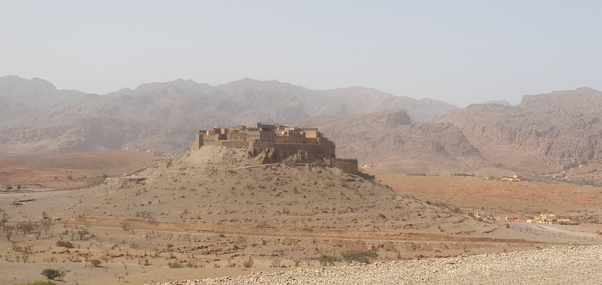 Kasbah auf einem Hügel vor einer trockenen Berglandschaft in Marokko.