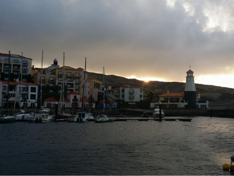 Hafen mit Segelbooten, Leuchtturm und bunten Häusern vor Hügeln bei Sonnenuntergang auf den Kanaren.