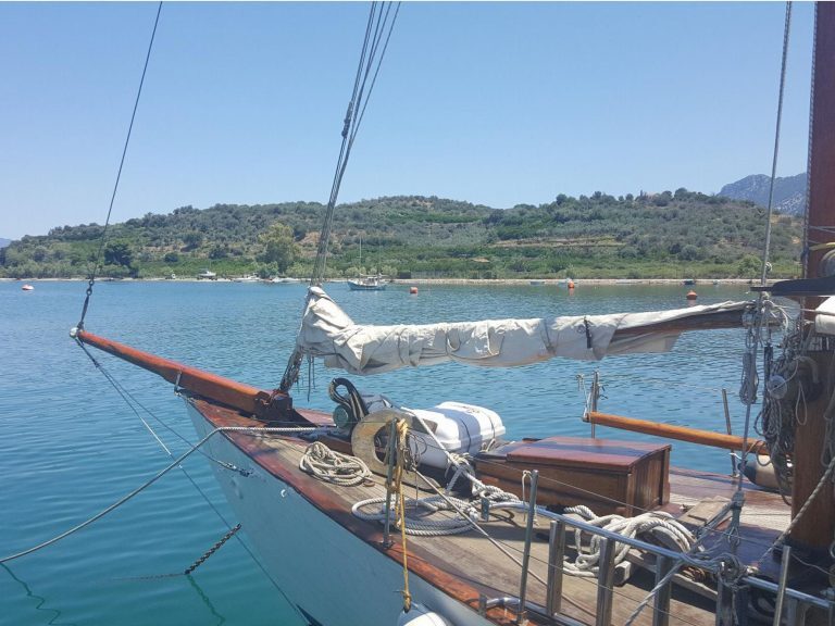 Segelboot mit eingerolltem Segel liegt vor Anker in einer Bucht an der grünen Küste Griechenlands.