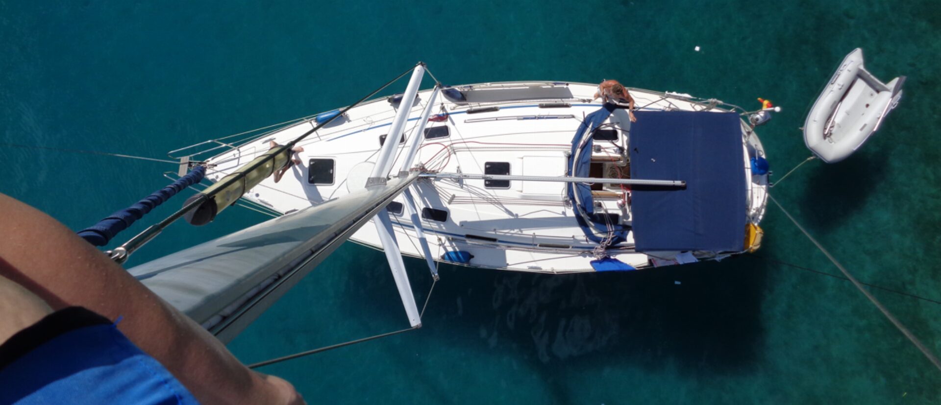 Segelboot von oben im türkisfarbenen Wasser des Mittelmeers, daneben ein Beiboot, eine Person liegt an Deck.